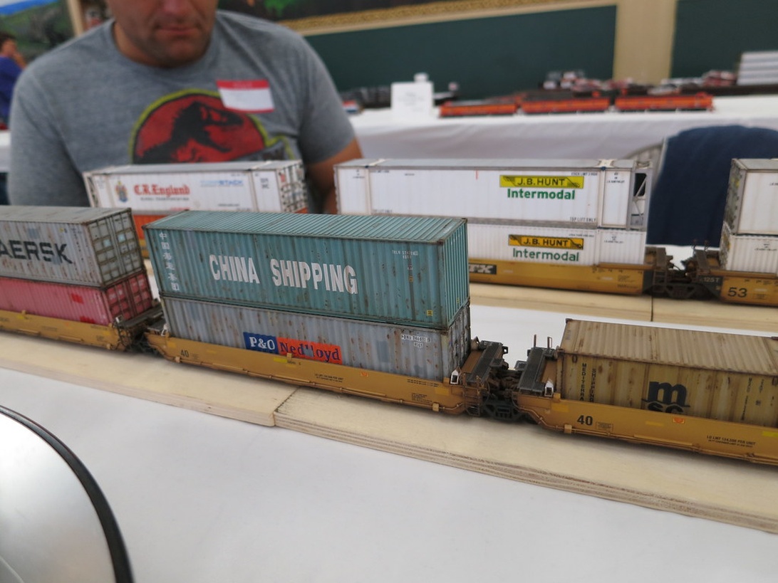 Hochwertige Modellbahn-Flachwagen, beladen mit Miniatur-Schiffscontainern von China Shipping, P&O Nedlloyd und anderen Marken. Zeigt realistische intermodale Güterverkehrsabläufe in detaillierter Modellbauweise.